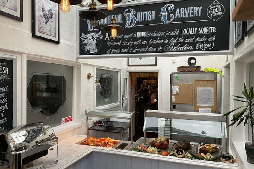 A British Carvery restaurant with a chalkboard menu, a grill station, and a variety of food displayed. 3