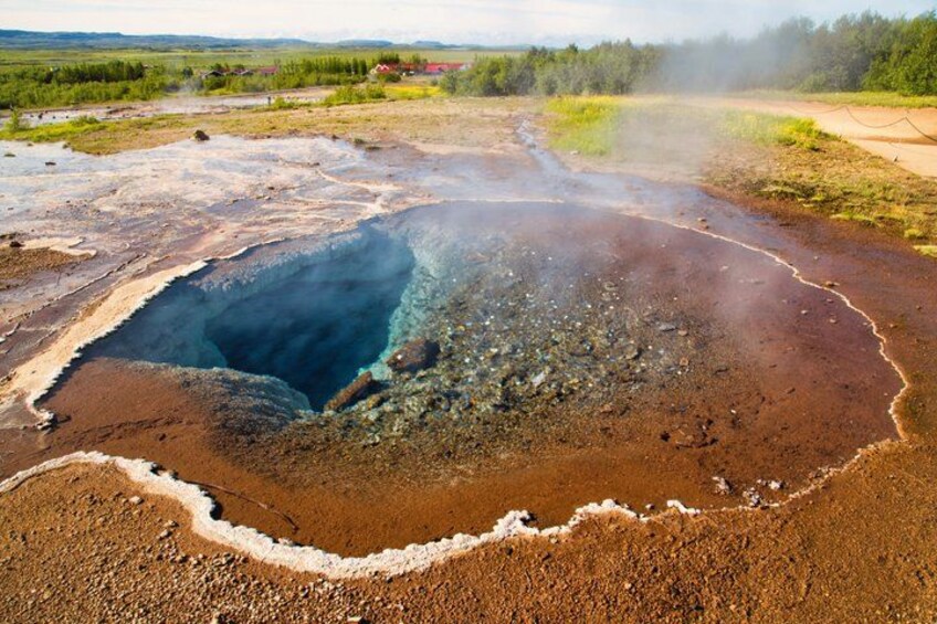 A geothermal area with a large crater, steam, and surrounding terrain. 3