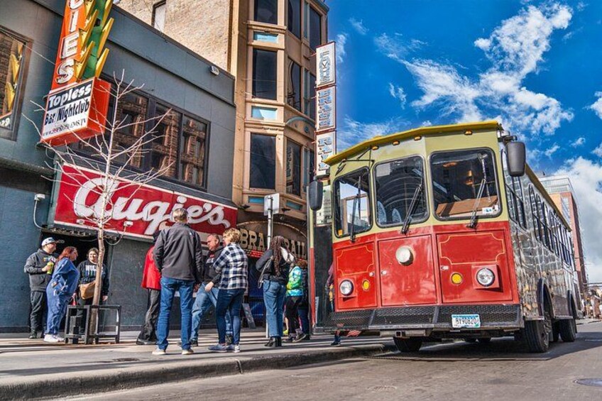 A vintage red and yellow bus on a city street, pedestrians on the sidewalk, and a building with a 'Topless Bar Nightclub' sign. 3