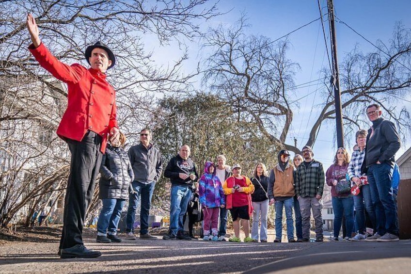 A person in a red jacket standing with arms raised, a group of people standing behind them, and leafless trees in the background. 4