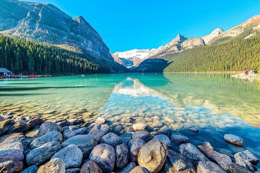 A clear lake with rocky shore, surrounded by mountains and dense forest. 3