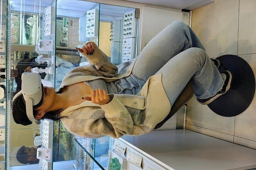 A person lying on a chair in a room with a glass partition, wearing a sweater and jeans. 1