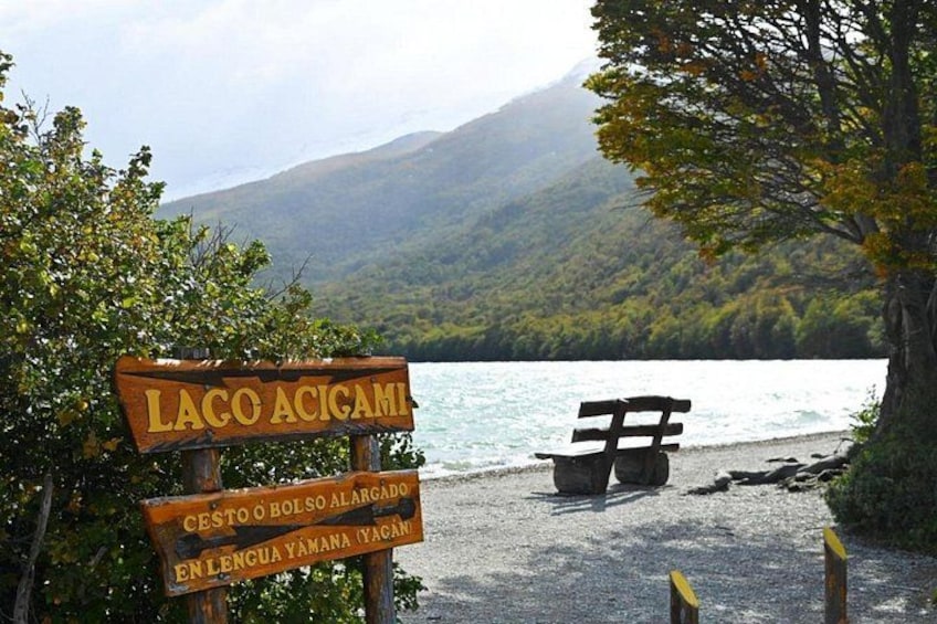 A wooden sign with 'Lago Acigami' and a bench by a lake. 5