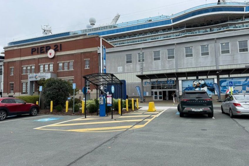 Ein Parkplatz mit Autos, eine Bushaltestelle und ein Gebäude mit der Beschriftung 'PIER 21'. 2