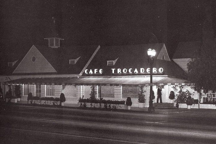Un caffè chiamato 'Cafe Trocadero' con tavoli all'aperto e una persona in piedi vicino all'ingresso. 4