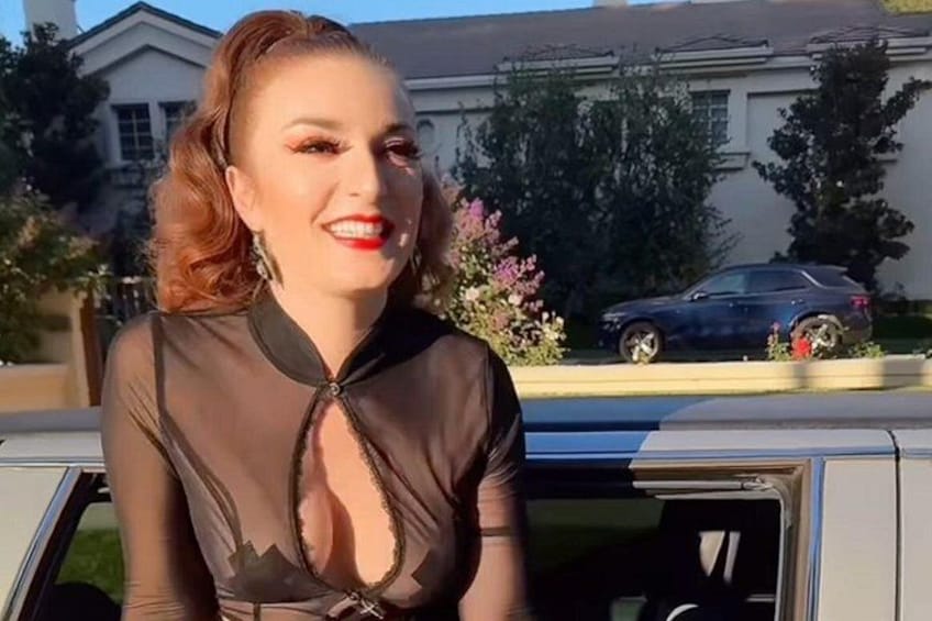 Una persona con un abito nero seduta in un veicolo, con una casa e un'auto sullo sfondo. 1