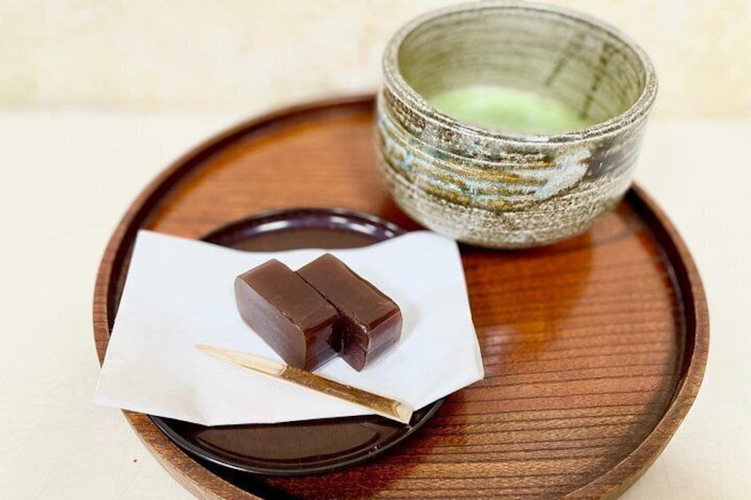 A piece of dark chocolate on a white napkin on a wooden tray, accompanied by a ceramic cup with a greenish glaze. 3