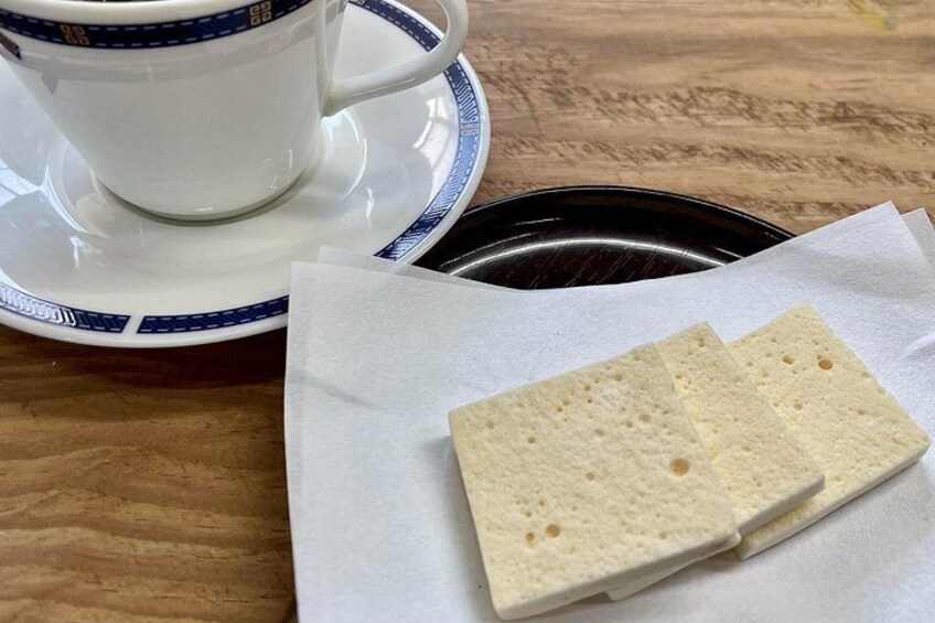 A white cup with a blue rim on a saucer, a black plate, and two square crackers on a white napkin. 5
