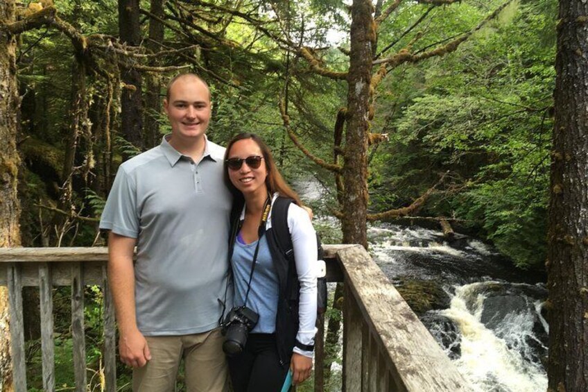 A man and woman standing on a wooden bridge with a waterfall in the background. 3