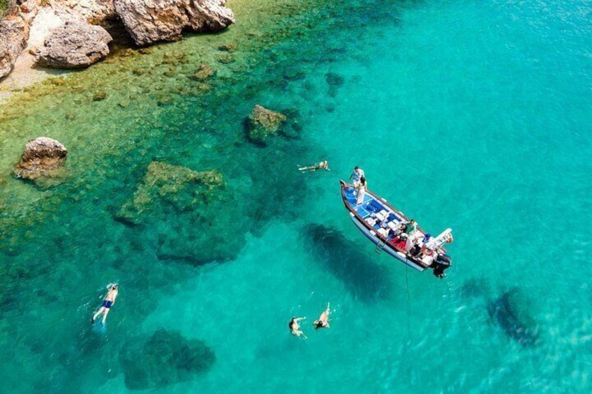 A boat with people swimming in clear turquoise water near rocks. 5