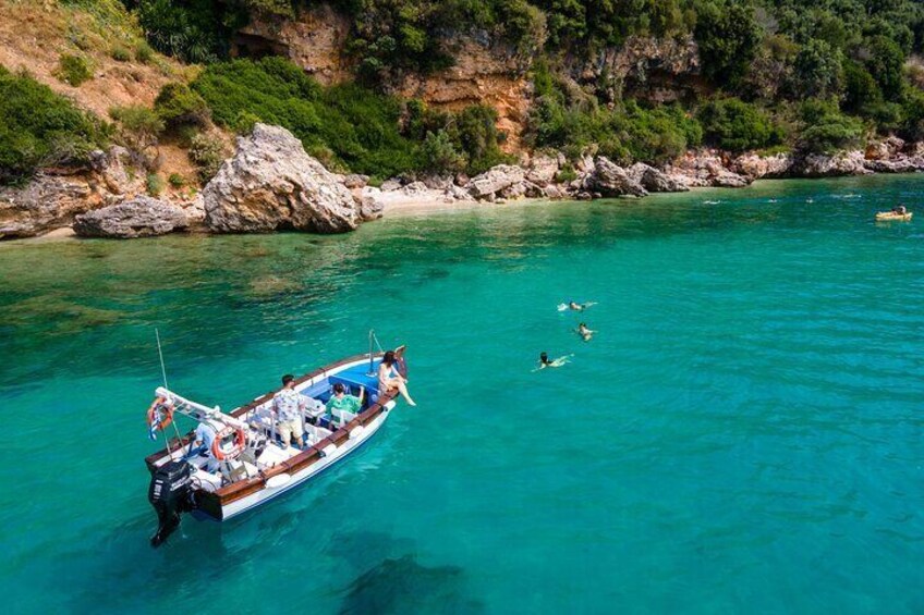 A boat with people swimming in clear turquoise water near rocky cliffs. 1