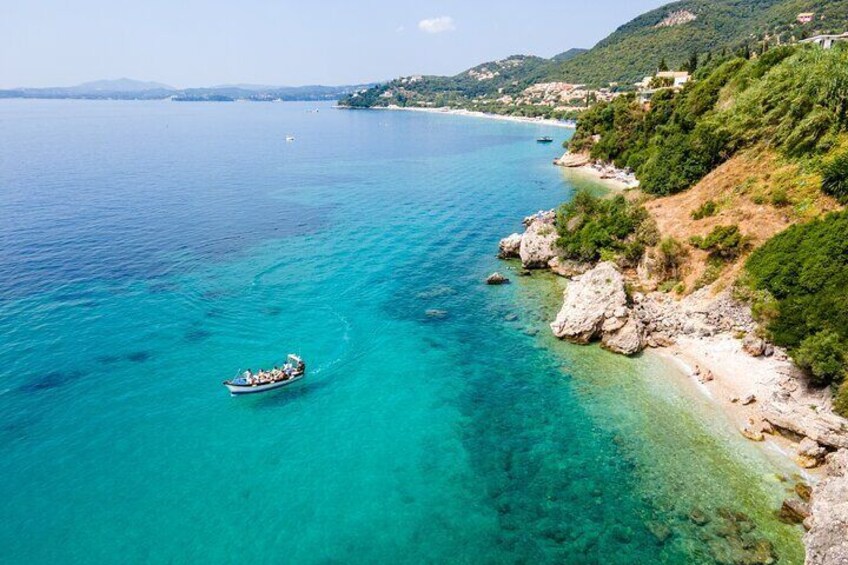 A boat on turquoise waters near a rocky coastline with greenery. 2