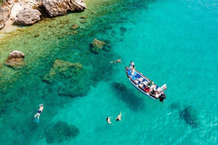 A boat with people swimming in clear turquoise water near rocks. 3