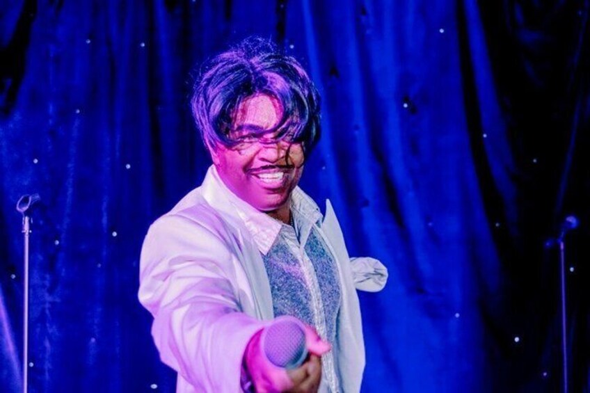 A person holding a microphone on a stage with a dark blue curtain backdrop. 5