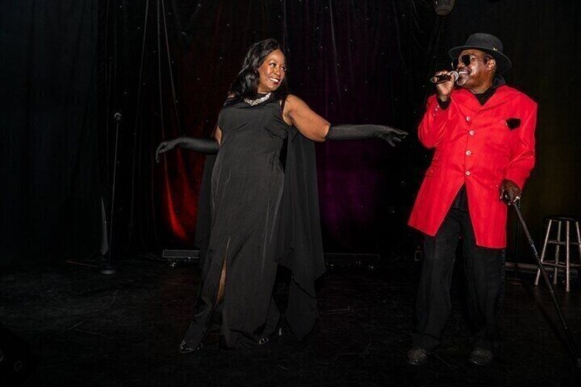 Two people on a stage, one in a black dress and the other in a red jacket. 3