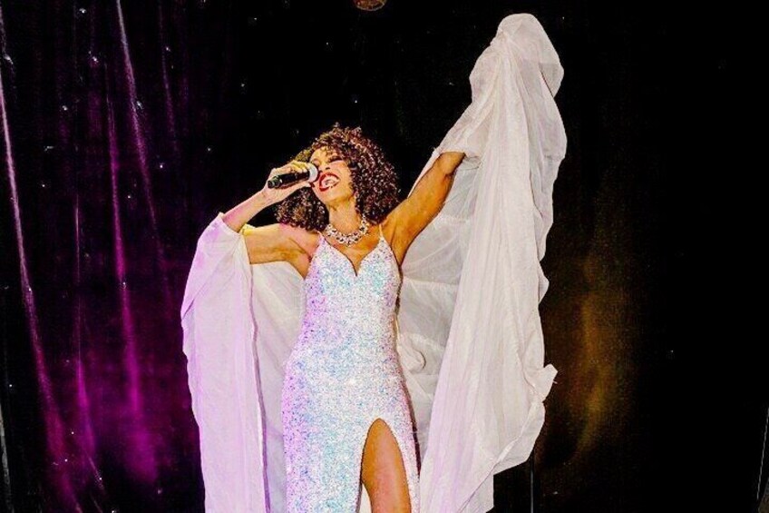 A person in a sparkling dress with a high slit, holding a microphone, and a white cape or shawl. 4