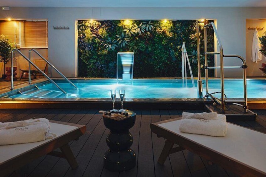 Une piscine extérieure chauffée agrémentée d’une cascade, entourée d’une terrasse en bois avec des sièges et d’un mur végétal tropical. 5