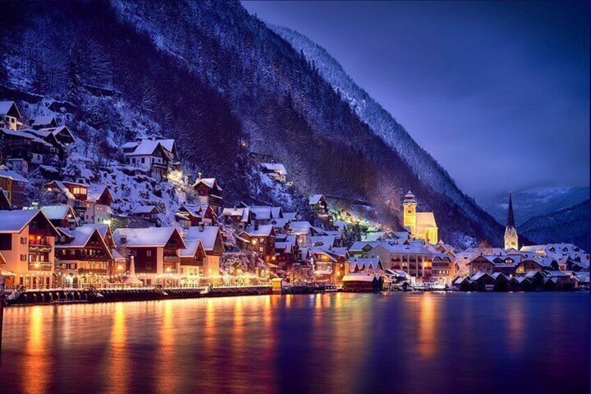 A snow-covered village with illuminated buildings and a church, surrounded by mountains. 2