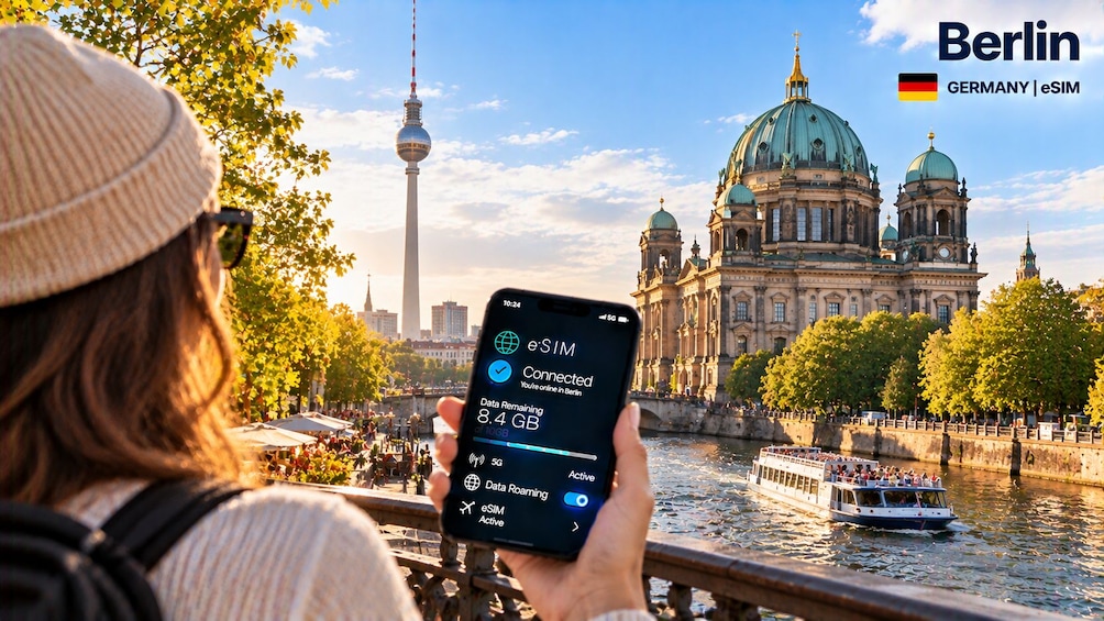 A person holding a smartphone with eSIM connectivity in Berlin, Germany, with landmarks like the Berlin TV Tower and the Brandenburg Gate visible in the background. 5
