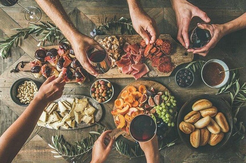 Eine Gruppe von Menschen sitzt an einem Holztisch mit verschiedenen Käsesorten, Fleisch, Oliven und Brot. 4