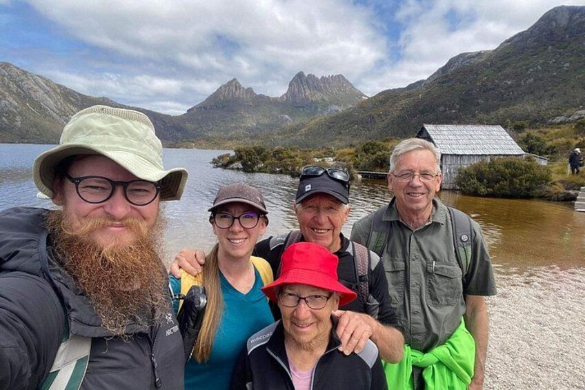 A group of people taking a selfie by a lake with mountains in the background. 1