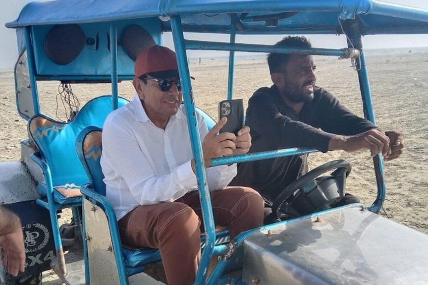 Two people in a blue vehicle on a sandy beach. 3