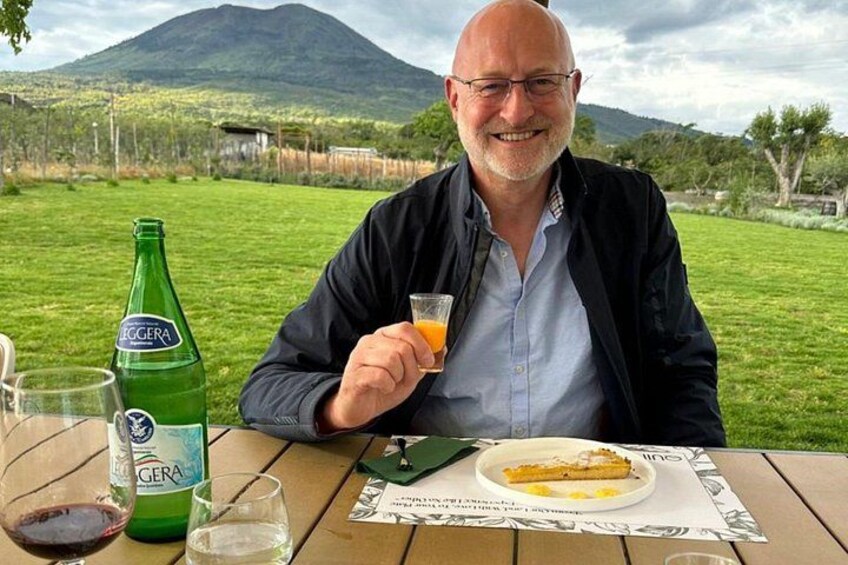 A man sitting at an outdoor table with a bottle of Cera, a glass of orange juice, and a plate of food. 2