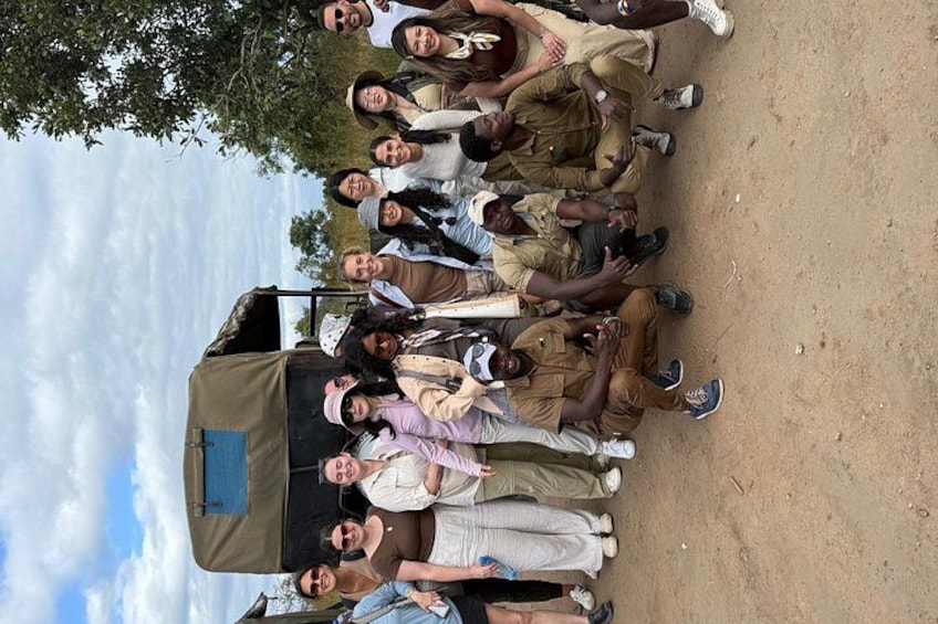 A group of people in uniform gathered around a vehicle on a dirt ground with trees and a cloudy sky in the background. 2