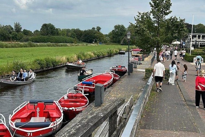 A canal with red boats docked, a walking path, and people walking. 2