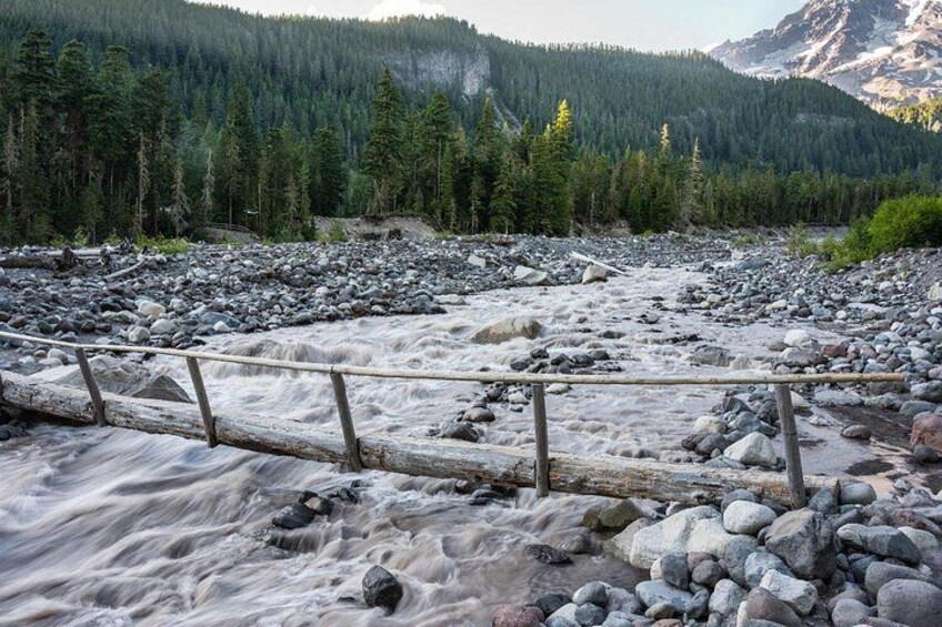 Un río con un puente de madera, rodeado por una cadena montañosa boscosa. 1