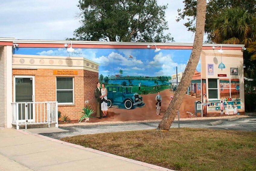 Une fresque murale ornant un bâtiment et représentant une voiture ancienne, un couple et un cycliste. 2