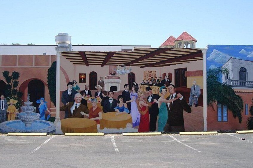 A mural with a group of people under a pergola, a fountain, and buildings in the background. 5