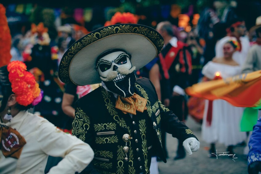 Une personne déguisée en squelette, portant un grand sombrero, se trouve au milieu d’une foule lors d’un événement festif. 1