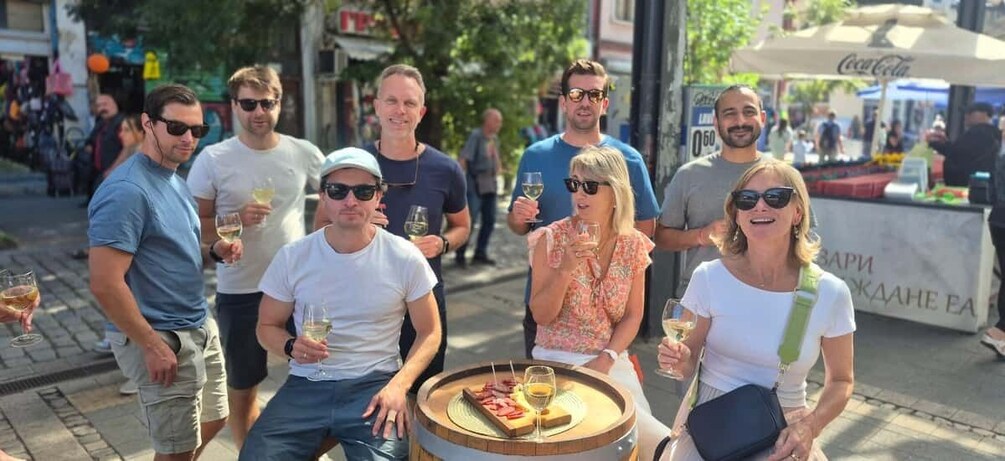 A group of people standing around a barrel with a tray of food and drinks. 1