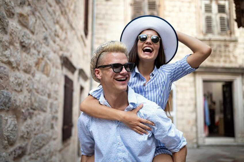 A man carrying a woman on his back in a narrow street with stone buildings. 1