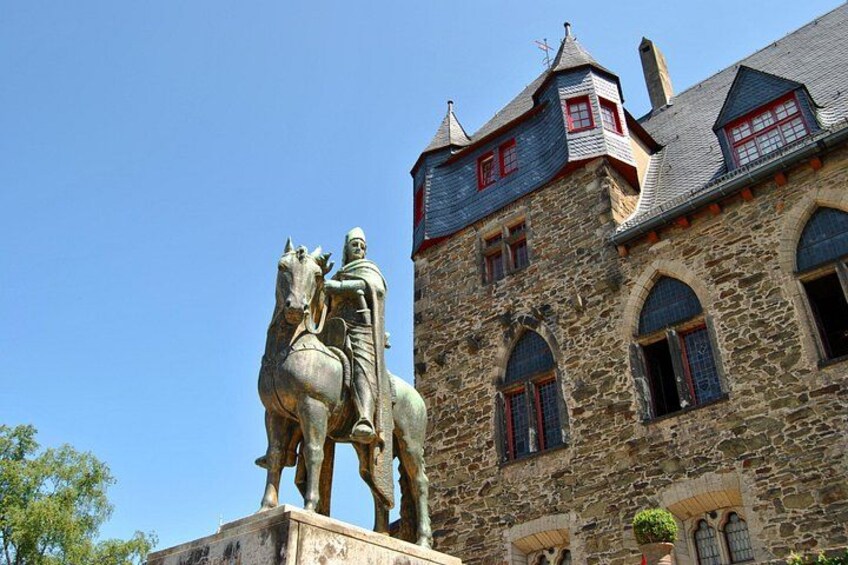 A stone building with a statue of a man on horseback, arched windows, and a red-tiled roof. 4