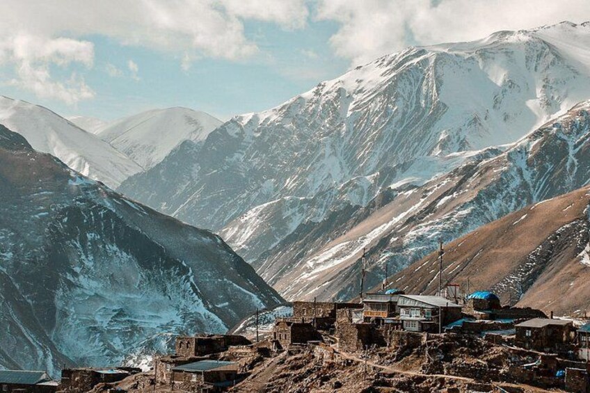 A mountainous landscape with snow-covered peaks, a small settlement with buildings, and a clear sky. 3