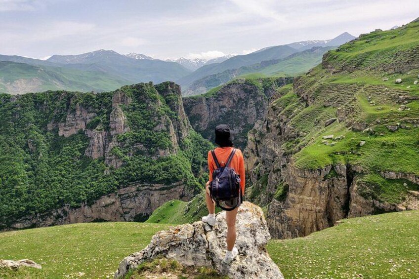A person standing on a rock with a backpack, overlooking a valley with cliffs and greenery. 2