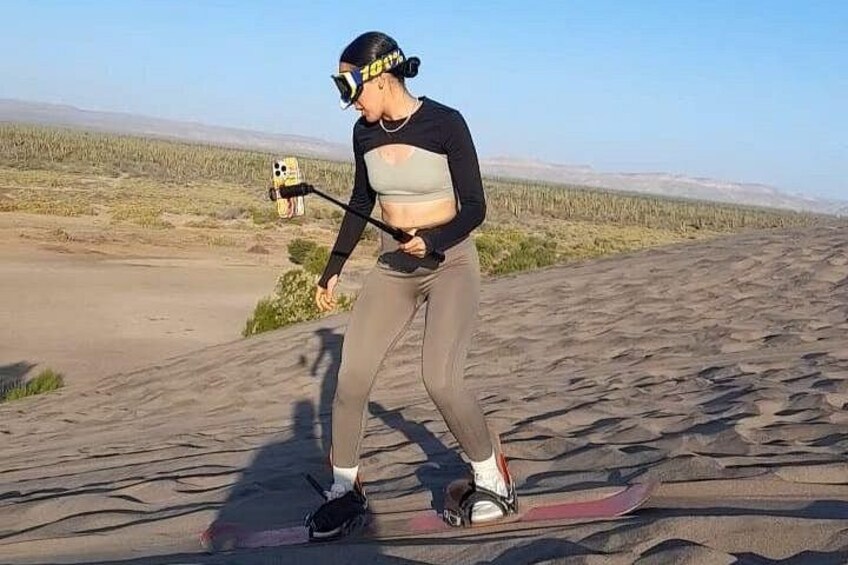 A person on a red snowboard, holding a selfie stick, in a desert landscape. 3