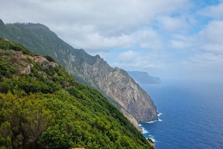 A coastal mountain landscape with dense green vegetation and steep cliffs overlooking the ocean. 1