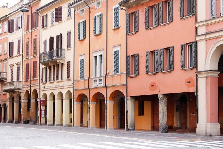 A street with multi-story buildings, some with balconies and arched doorways. 4