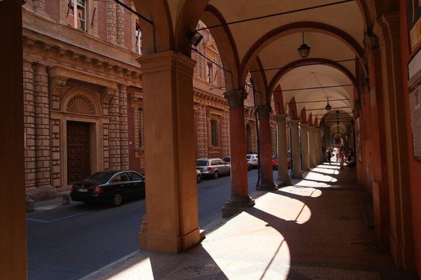 A covered walkway with arches, a street with parked cars, and a building with a red door. 3
