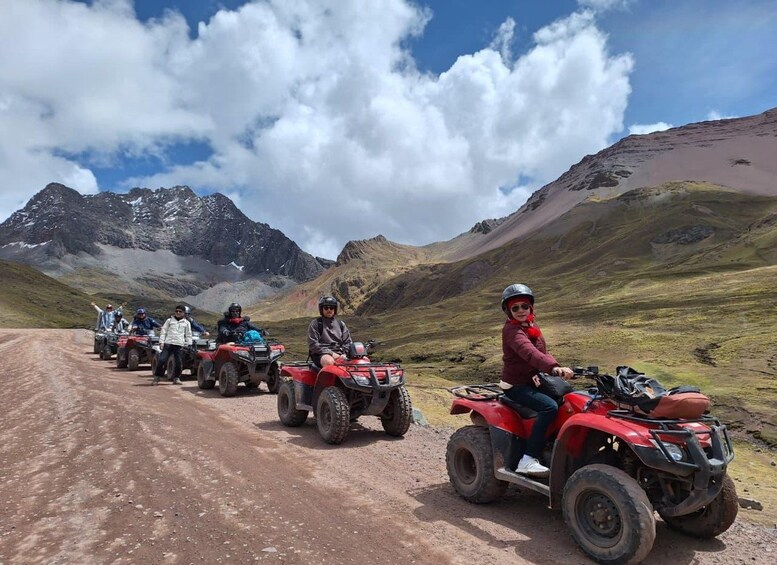 A group of people riding red all-terrain vehicles on a dirt road in a mountainous area with clear skies. 5
