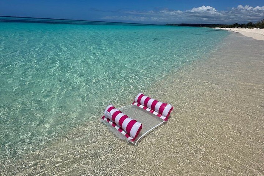 Une plage avec une eau turquoise cristalline et une chaise longue à rayures roses et blanches. 5