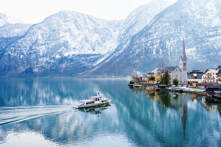 A boat on a calm lake with snow-capped mountains in the background and a church with a tall steeple. 1