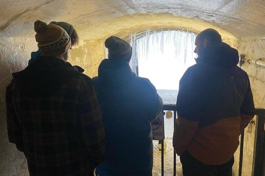 Drie personen in een schemerig verlichte, gewelfde constructie met een raam aan het einde. 4
