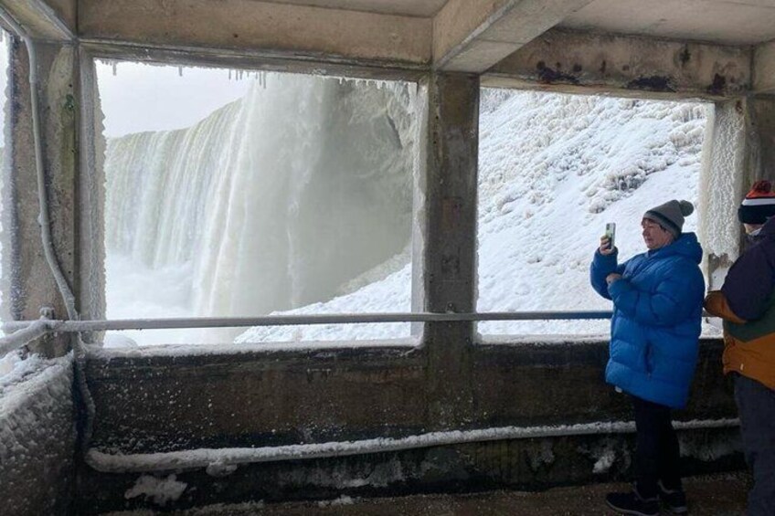 A person in a blue jacket taking a photo of a waterfall. 4