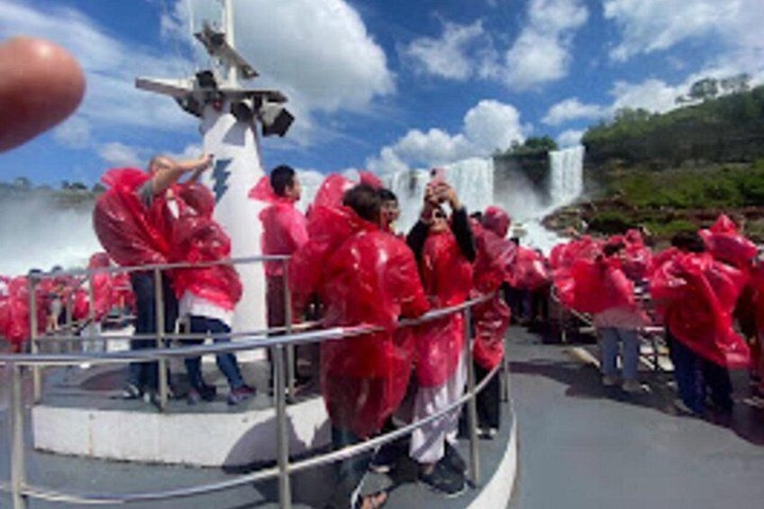 A group of people in red rain ponchos gathered around a water feature with a waterfall in the background. 4