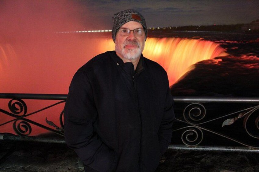 A man standing in front of a waterfall with a railing. 2