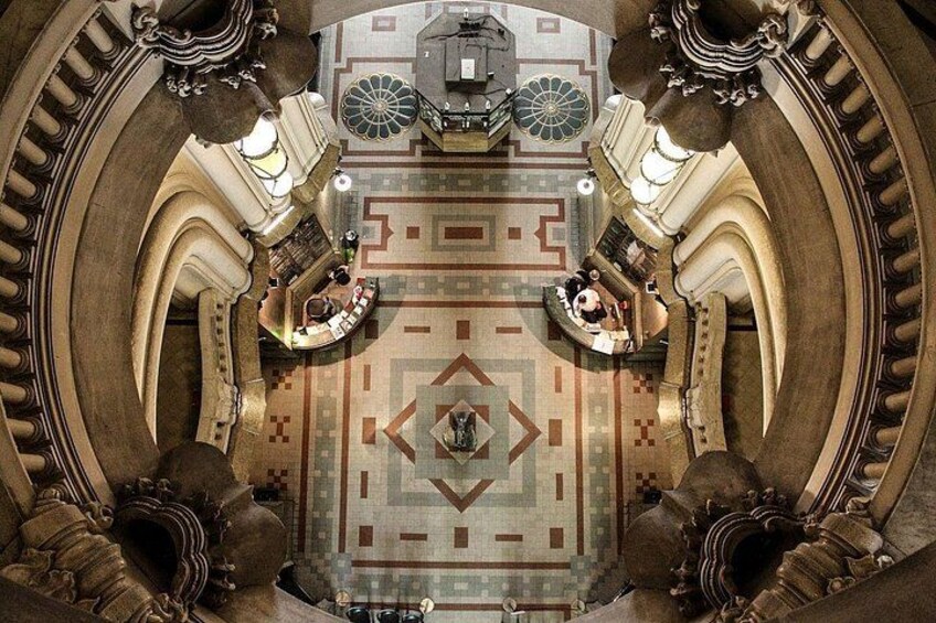 An ornate hall with a patterned floor, large columns, and a central chandelier. 4